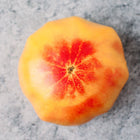 Top-down view of a Hillbilly tomato with golden-yellow skin and red marbling on a grey textured surface.