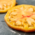 Two thick slices of golden Hillbilly tomato with red marbling resting on a dark, textured surface.