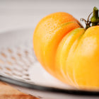 A large, glowing orange Kellogg's Breakfast beefsteak tomato with water droplets resting on a white decorative plate.
