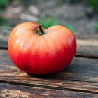 A large, ripe Pink Brandywine tomato with rose-pink skin resting on a weathered wooden surface.