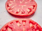 Two thick, juicy slices of a Pink Brandywine tomato with deep rose-pink flesh on a light gray surface.