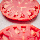 Two thick, juicy slices of a Pink Brandywine tomato with deep rose-pink flesh on a light gray surface.
