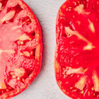 Two thick, juicy slices of a Pink Brandywine tomato showing deep rose-pink, meaty flesh and scattered seeds.