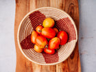 Fresh San Marzano tomatoes in a woven basket with red and tan patterns, resting on a wooden cutting board.