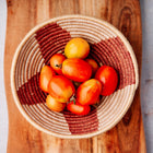 Fresh San Marzano tomatoes in a woven basket with red and tan patterns, resting on a wooden cutting board.