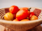 Freshly harvested red San Marzano tomatoes in a woven bowl on a wooden surface.