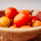 Freshly harvested red San Marzano tomatoes in a woven bowl on a wooden surface.
