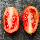 Two halves of a red, plum-shaped Italian Roma tomato showing meaty flesh and seeds on a dark, textured surface.