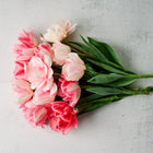 A bouquet of Foxtrot double tulips with pink and crimson petals and green stems on a light textured background.