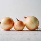 Three Walla Walla sweet onions with light brown papery skins sitting on a white wooden surface.