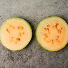 Two round slices of Tendersweet Orange watermelon showing glowing orange flesh and seeds on a gray surface.