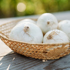 White Sweet Spanish onions in a woven wicker basket on a wooden surface.