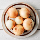 Six Yellow Sweet Spanish onions with golden-brown skins arranged on a decorative ceramic plate.