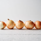 Five harvested Yellow Sweet Spanish onions with golden-brown skins lined up on a white wooden surface.