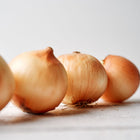 Several Yellow Sweet Spanish onions with golden-brown papery skins arranged on a white wooden surface.
