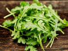 Fresh, deeply cut green leaves of Wild Rocket arugula resting on a rustic dark wooden surface.