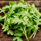 Fresh, deeply cut green leaves of Wild Rocket arugula resting on a rustic dark wooden surface.