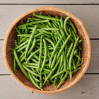Freshly harvested Blue Lake 274 bush beans in a round woven basket on a grey wooden surface.