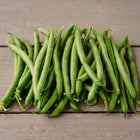 A pile of freshly harvested, straight, medium-green Blue Lake 274 bush bean pods on a rustic wooden surface.
