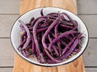 Royalty Purple Pod bush beans piled in a white enamel colander on a wooden board.