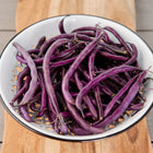 Royalty Purple Pod bush beans piled in a white enamel colander on a wooden board.