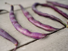 Several deep violet Royalty Purple Pod bush beans laid out on a weathered wooden surface.