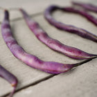 Several deep violet Royalty Purple Pod bush beans laid out on a weathered wooden surface.