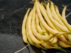 A pile of fresh, bright yellow Golden Wax bush beans resting on a dark, veined marble surface.
