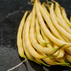 A pile of fresh, bright yellow Golden Wax bush beans resting on a dark, veined marble surface.