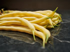 A pile of fresh, bright yellow Golden Wax bush bean pods resting on a dark, polished marble surface.