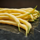 A pile of fresh, bright yellow Golden Wax bush bean pods resting on a dark, polished marble surface.