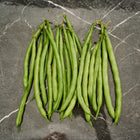 A cluster of long, slender, deep green Jade bush bean pods arranged on a dark gray marble surface.
