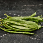 A pile of fresh, long green Kentucky Wonder pole bean pods resting on a dark marble surface.