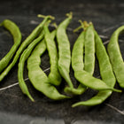 Freshly harvested green Kentucky Wonder pole bean pods lying on a dark marble surface.