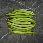A pile of fresh, smooth, medium-green Provider bush bean pods arranged on a dark, textured marble surface.