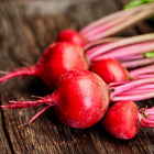 Freshly harvested Chioggia beets with vibrant red skins and pink-striped stems on a rustic wooden surface.