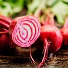Sliced Chioggia beet showing pink and white candy-striped rings next to whole beets on a rustic wooden surface.