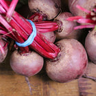 Bundles of harvested Detroit Dark Red beets with vibrant red stems and round, dark roots on a wooden surface.