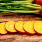 Golden Detroit beet slices with bright yellow flesh and green stems on a wooden cutting board.
