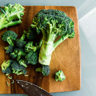 Freshly cut Waltham 29 broccoli florets and stalks arranged on a wooden cutting board with a kitchen knife.