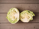 Two halves of a freshly cut Early Jersey Wakefield cabbage showing pale green, tightly packed layers on a rustic wooden surface.