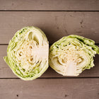 Two halves of a freshly cut Early Jersey Wakefield cabbage showing pale green, tightly packed layers on a rustic wooden surface.