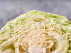 Close-up of a halved Early Jersey Wakefield cabbage showing its pale green, tightly layered leaves and cone-shaped structure.