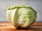 Late Flat Dutch cabbage head with pale green leaves and water droplets on a wooden cutting board.