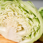 Cross-section of a Late Flat Dutch cabbage showing dense, pale green layers and ruffled leaves on a wooden surface.