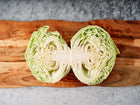 Late Flat Dutch cabbage cut in half, showing dense pale green layers on a rustic wooden cutting board.