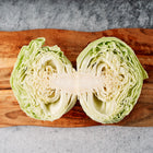 Late Flat Dutch cabbage cut in half, showing dense pale green layers on a rustic wooden cutting board.