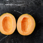 Two halves of a Delicious 51 cantaloupe with orange flesh on a dark marble surface.