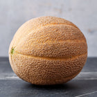 Hale’s Best Jumbo cantaloupe with heavy tan netting on a dark marble surface against a gray background.