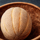 Hale’s Best Jumbo cantaloupe with heavy netting resting in a round, woven brown wicker basket.